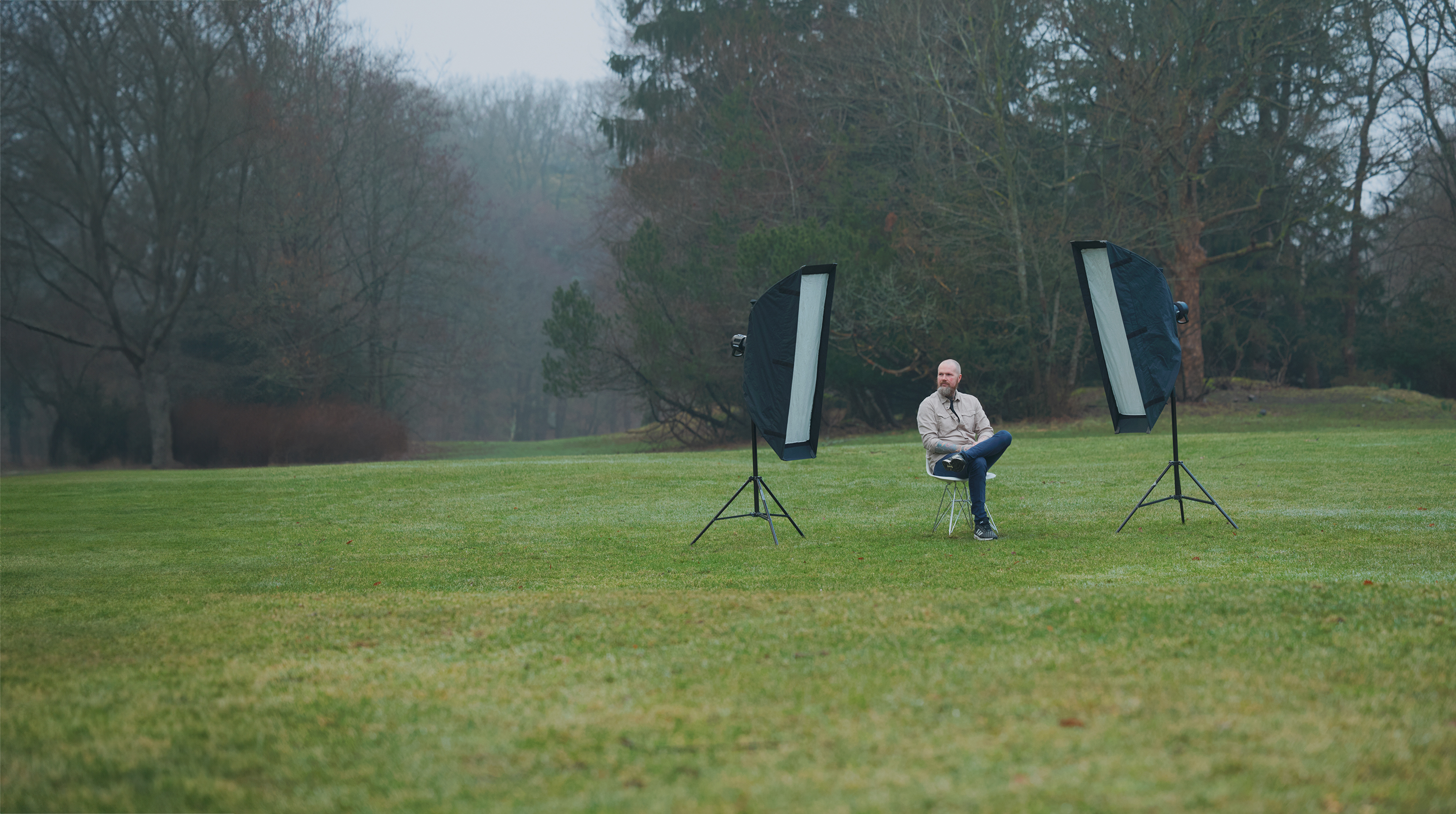 A man sitting in a chair in a field with studio lights.