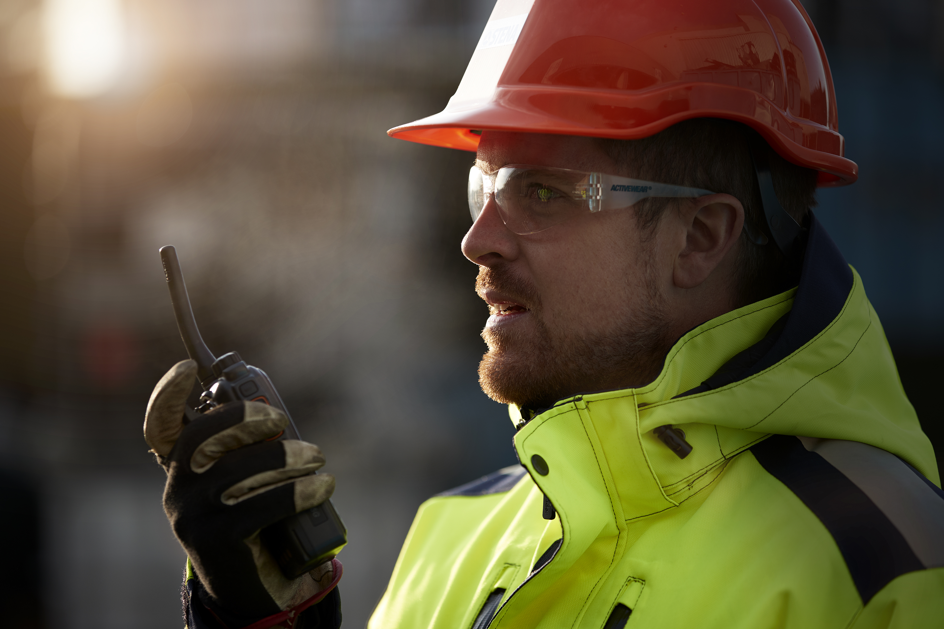 A close-up image of a Stena Metall Group employee in hi-vis protective gear talking into a walkie-talkie.