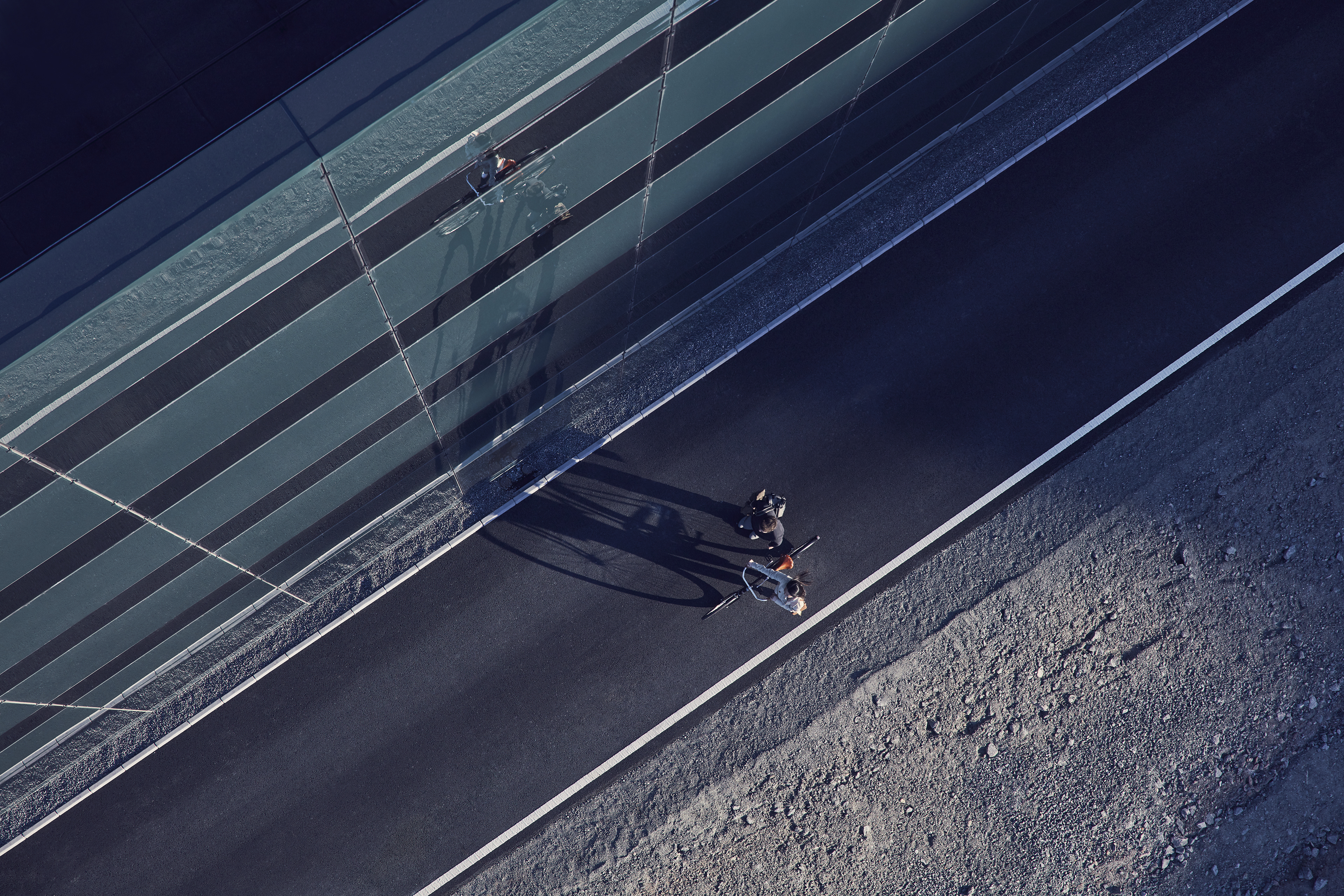 Two pedestrians walking through a city, one with a bike and one without.