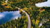 An aerial shot of a road running through a Swedish forest beside a lake.