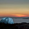 A small tent pitched on the Swedish west coast is illuminated as darkness falls.