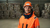 Close-up of a male Stena Recycling employee in hi-vis protective gear, standing in front of a piles with packaged paper waste 