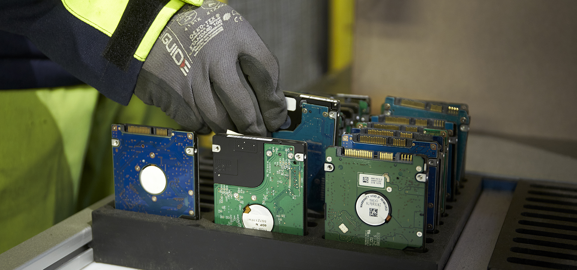 Närbild av en hand klädd i arbetshandske, som håller i elektronisk utrustning i en återvinningsmiljö