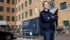 A male BatteryLoop employee stands in a courtyard, in the background a container and a car connected to an electric charger.