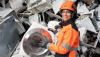 En kvinnlig Stena Recyclinganställd i skyddskläder, som står framför en hög med metallskrot och håller en bit av tvättmaskin