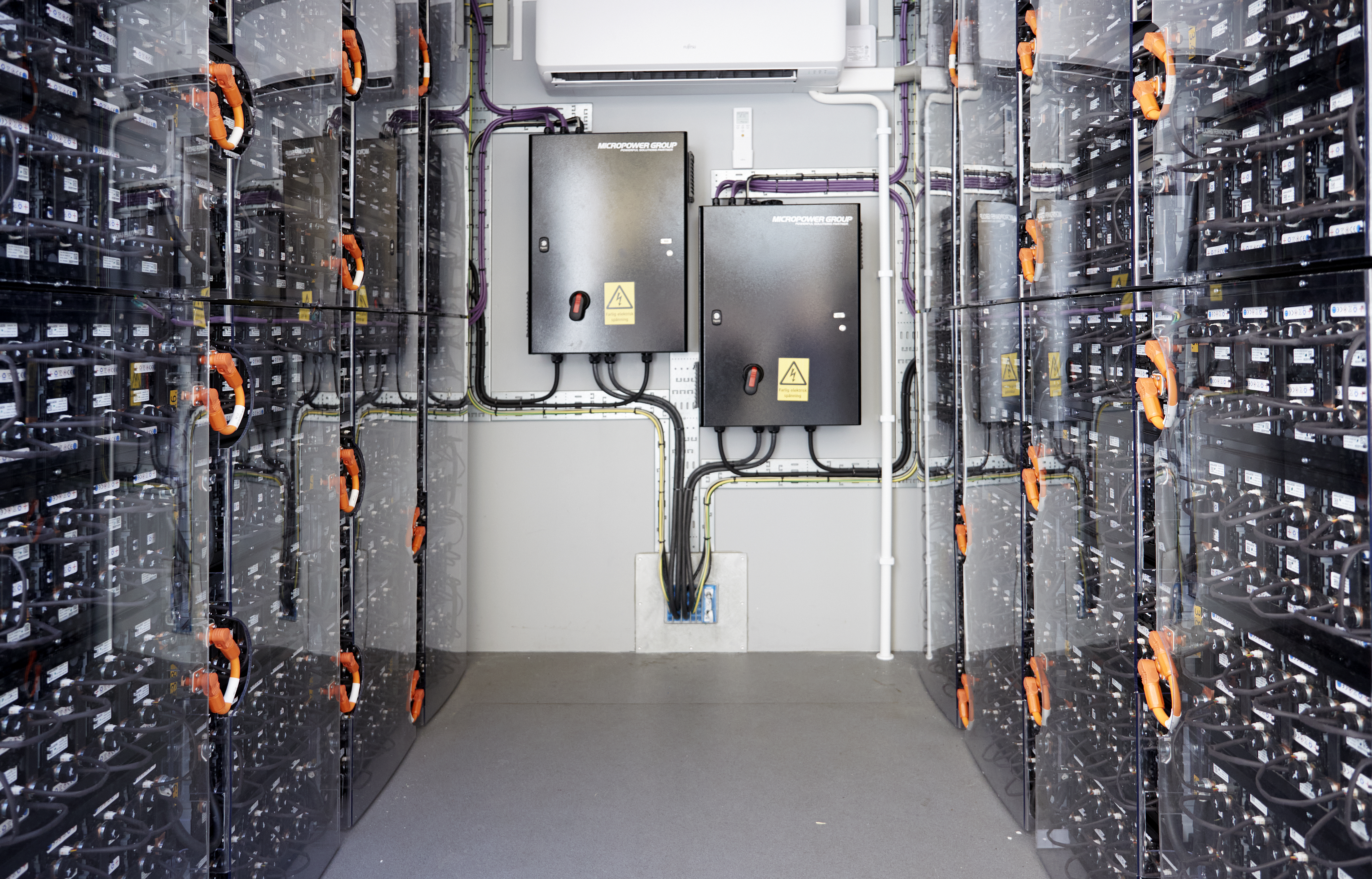 Inside of a container. Two black boxes hanging on the opposite wall. The surrounding walls are covered with rows of smaller boxes connected with cables.