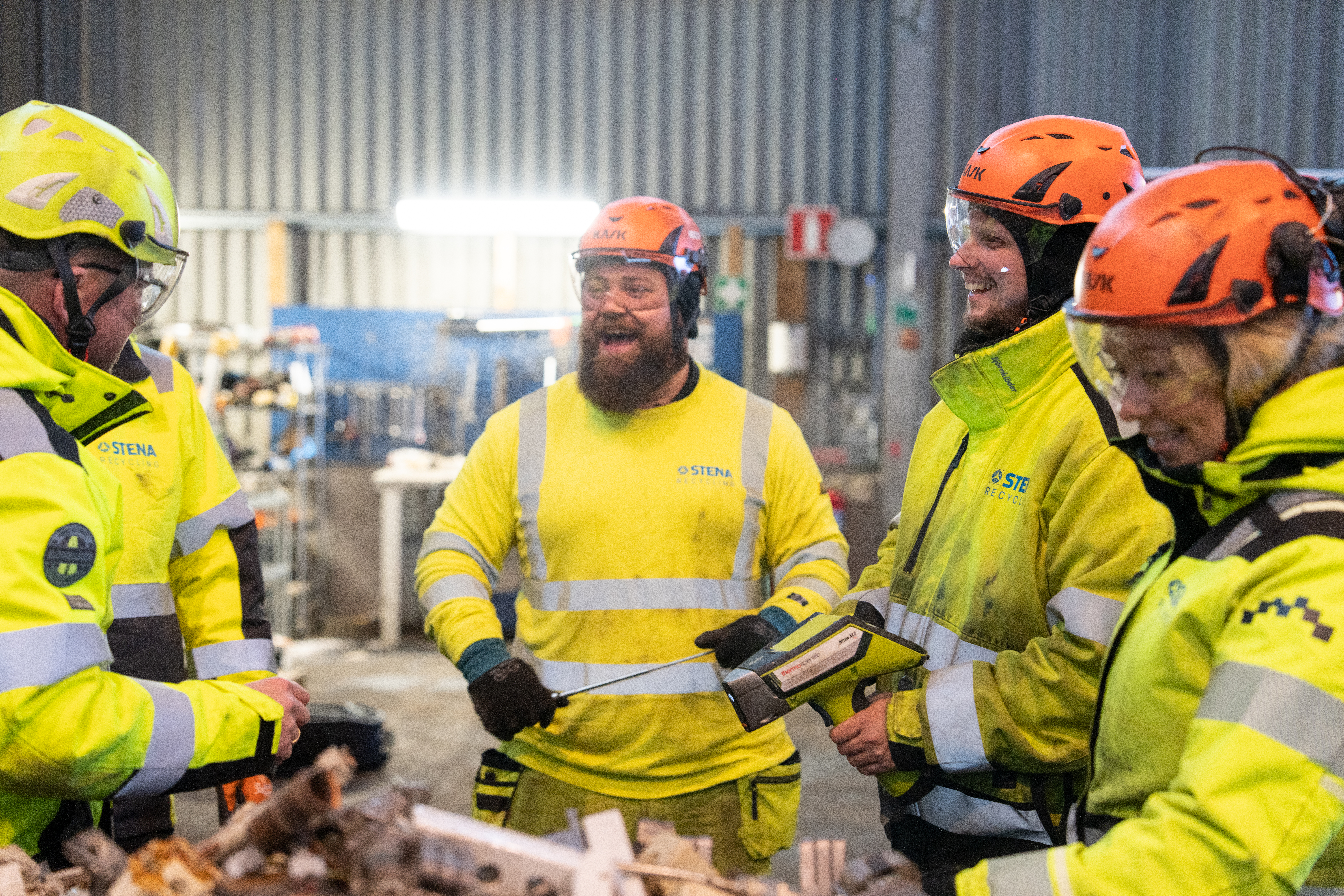 En grupp anställda på Stena Recycling, klädda i skyddsutrustning, undersöker metallskrot. 