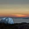 A small tent pitched on the Swedish west coast is illuminated as darkness falls.